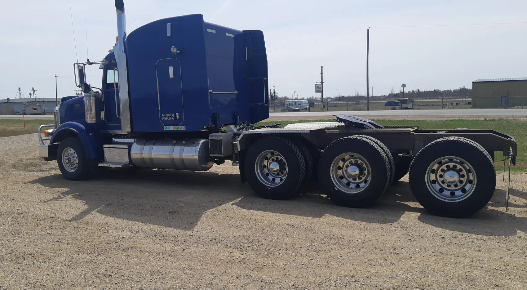 Blue tri-axle highway tractor on a gravel lot