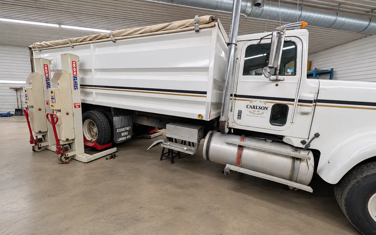 White grain truck raised on heavy-duty column lifts in the shop